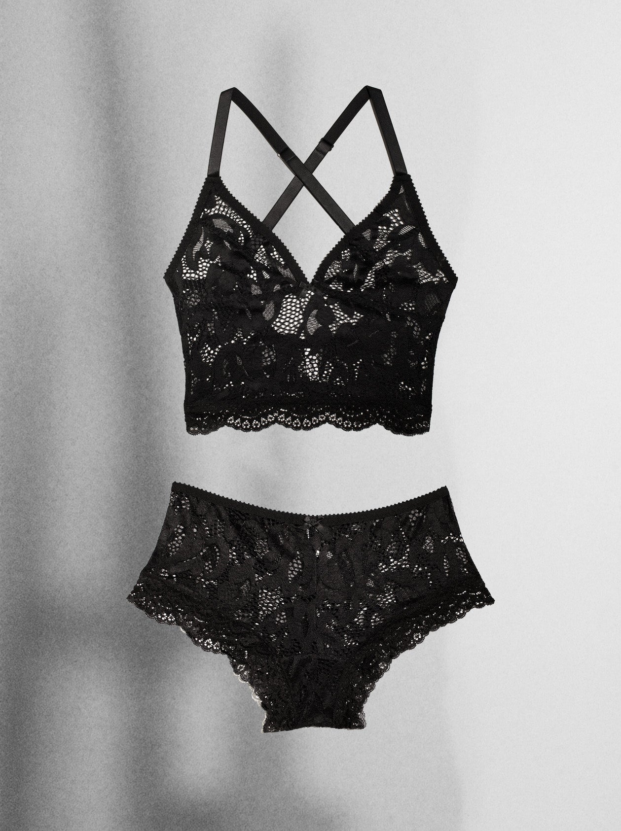 A two-piece black lace lingerie set featuring a strappy underwire bra and matching high-waisted briefs, displayed against a light gray background with soft shadows.